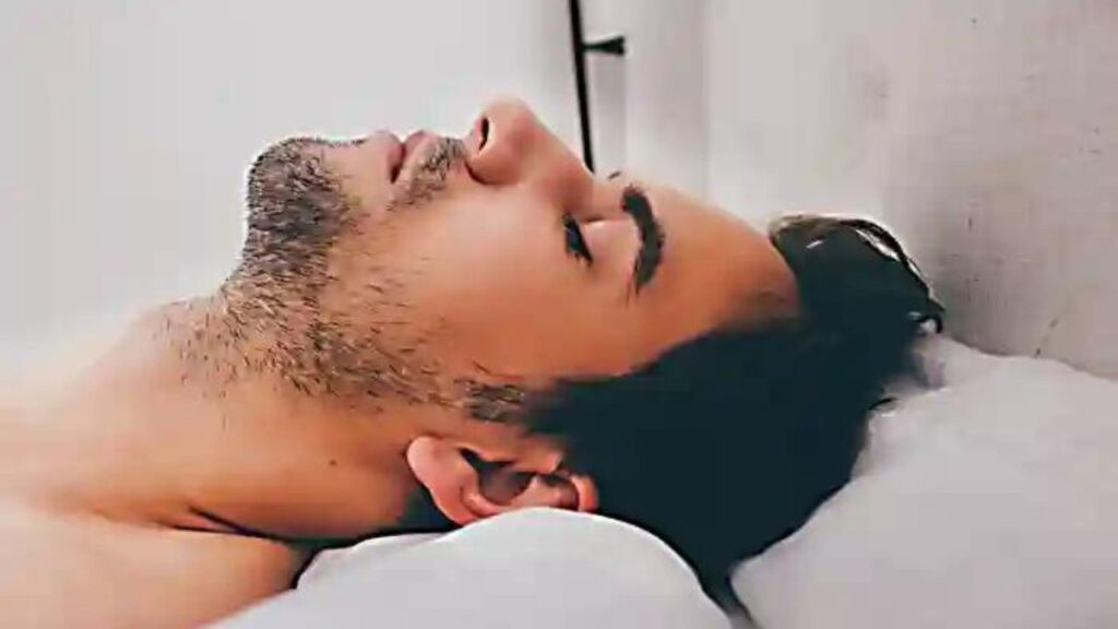 O Sono é Essencial para o nosso Bem-Estar? Na imagem, um rapaz está dormindo em sua cama, com lençóis brancos.