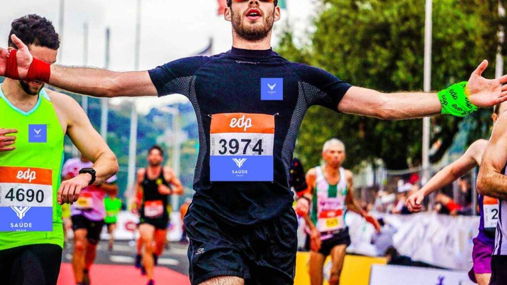 Uma disputa de corrida na rua no Brasil, vários atletas competindo, o rapaz de camiseta e calção azul-marinho de número 3974, ganha a corrida em primeiro lugar.