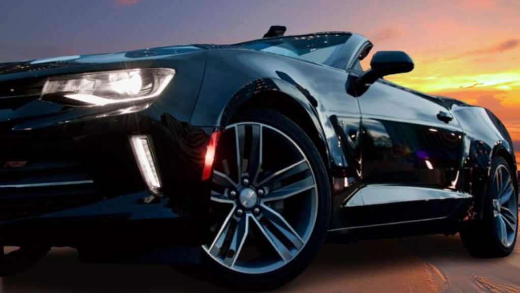 Alcance de Metas e Crescimento Pessoal. Na imagem, um lindo carro conversível, importado, na cor preta, parado numa estrada, ao fundo um opor do sol.