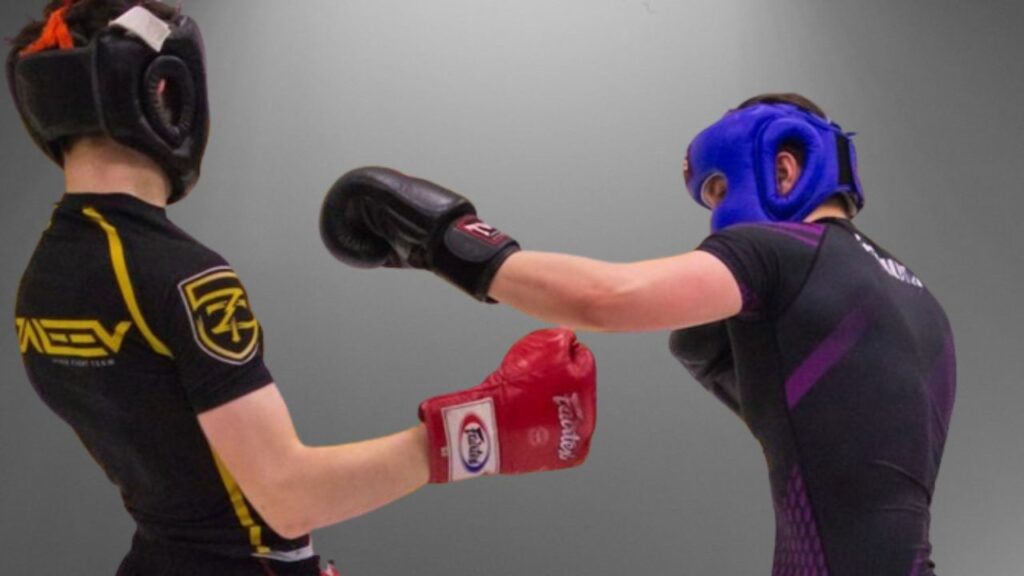 Praticar Luta: Guia Completo. Na imagem, dois rapazes vestidos com roupas próprias para luta, na cor preta, um com detalhes em amarelo, o outro com detalhes em roxo. Ambos estão usando os acessórios para proteção, como capacete e luvas.