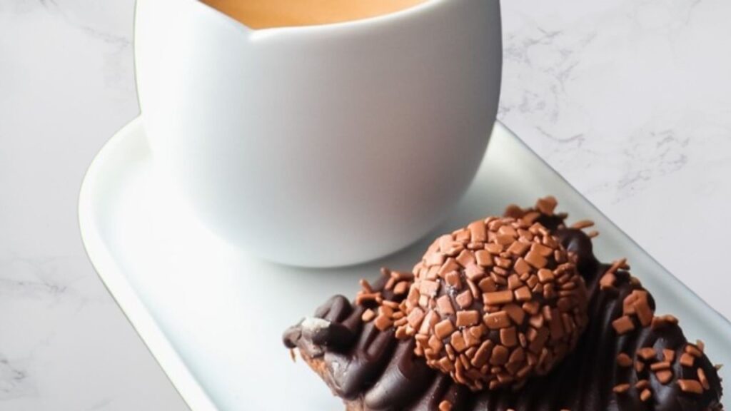 Brigadeiro Sem Açúcar: Uma Doçura Cheia de Sabor! A imagem mostra um brigadeiro suculento e uma xícara de café sobre um prato retangular. Todas as peças são em louça branca.